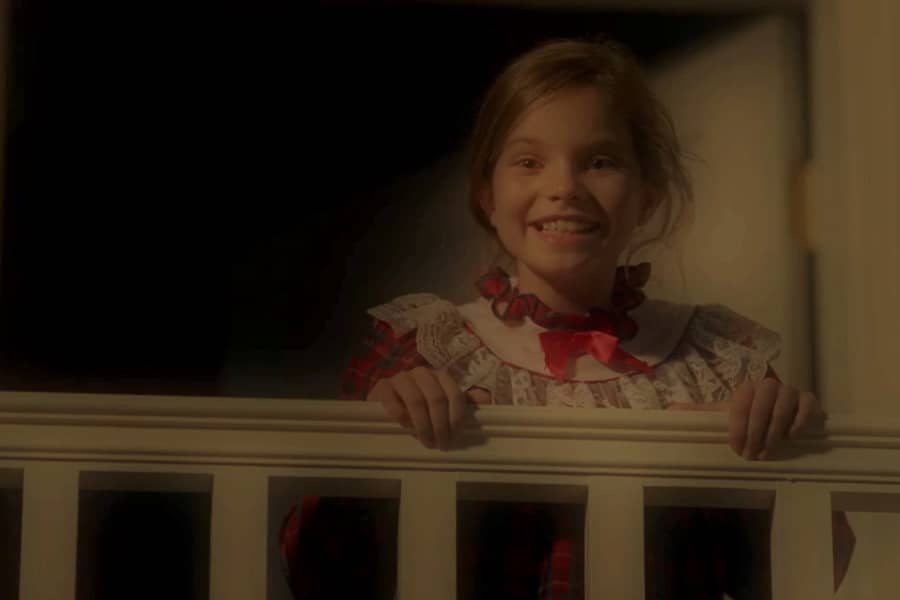 a young girl in a nightgown looks over the banister and smiles