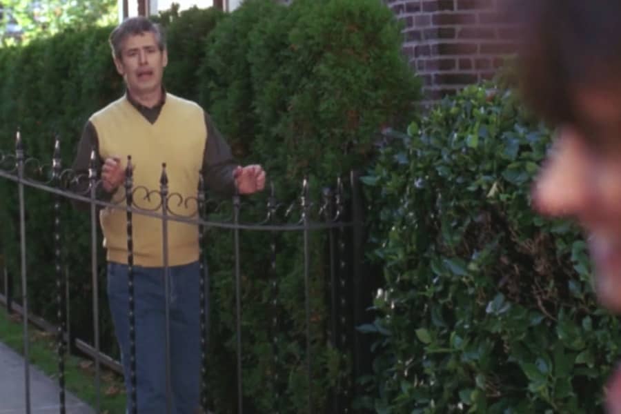 a man calls to another woman from behind a garden fence