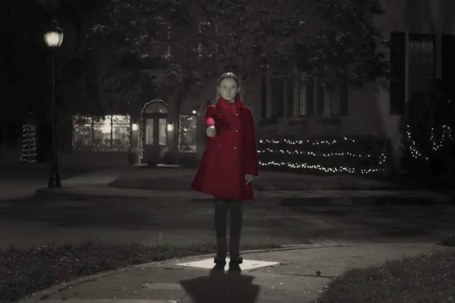 a black and white shot of a young girl pointing, her coat is bright red