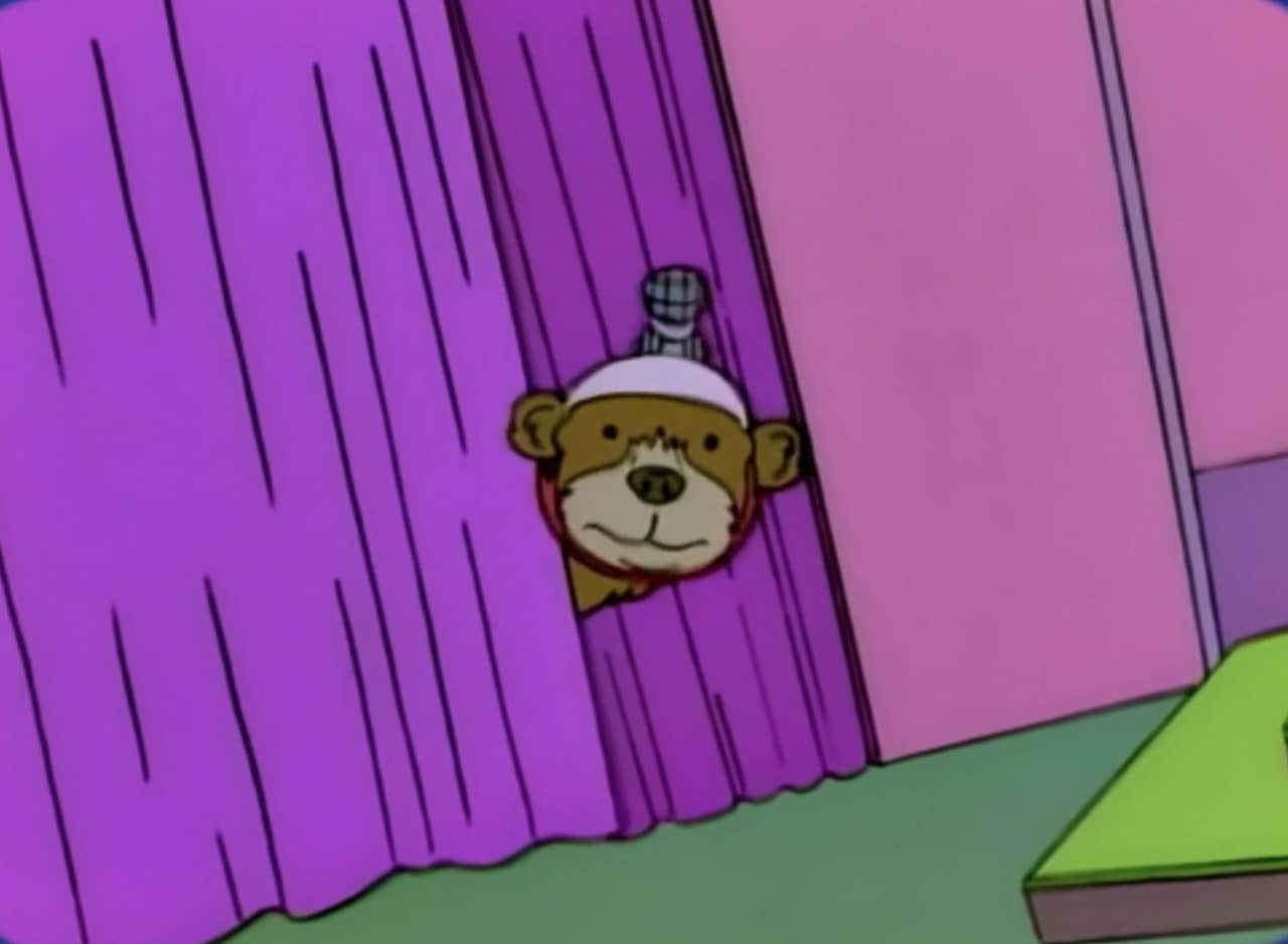 Gentle Ben, a brown bear with a microphone attached to its head peeks out from behind a curtain