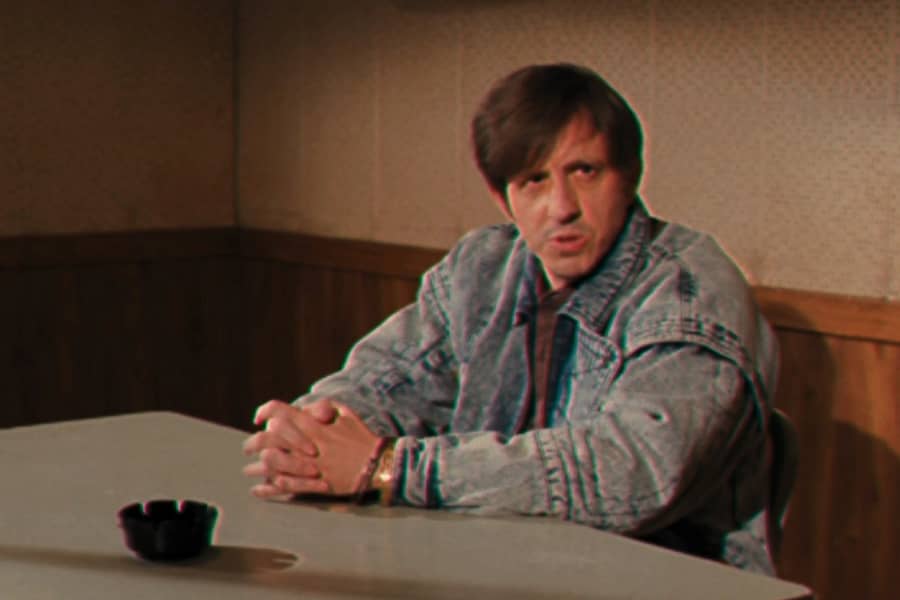 a man in handcuffs sits at an interrogation table