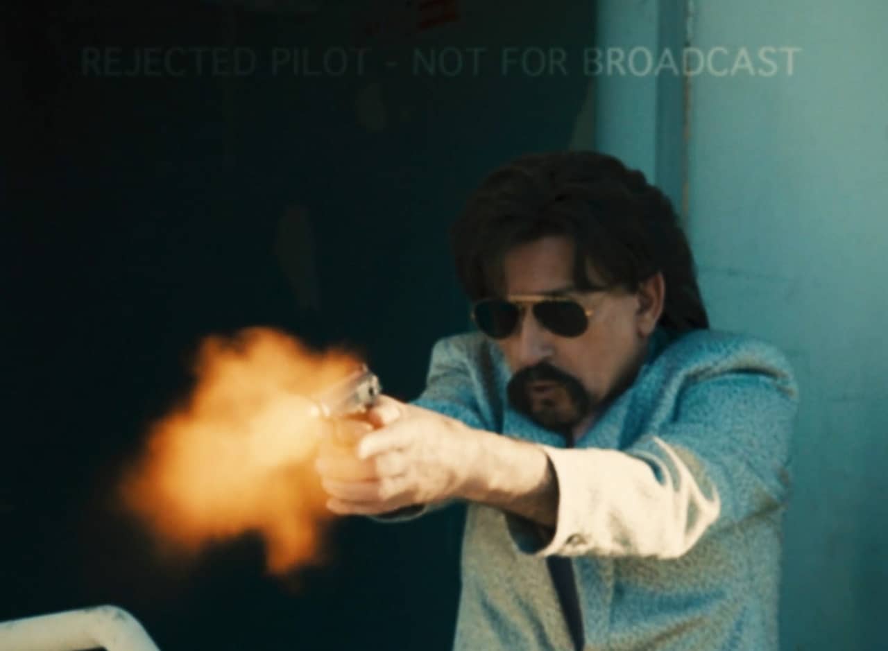 Trevor Slattery in suit and aviators shooting a gun