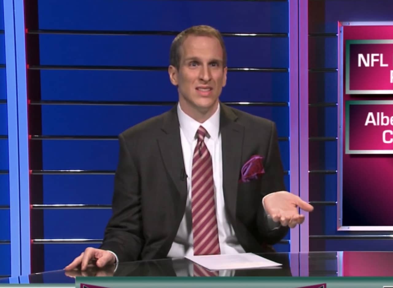 an anchor in a suit sits at a talk show desk looking confused