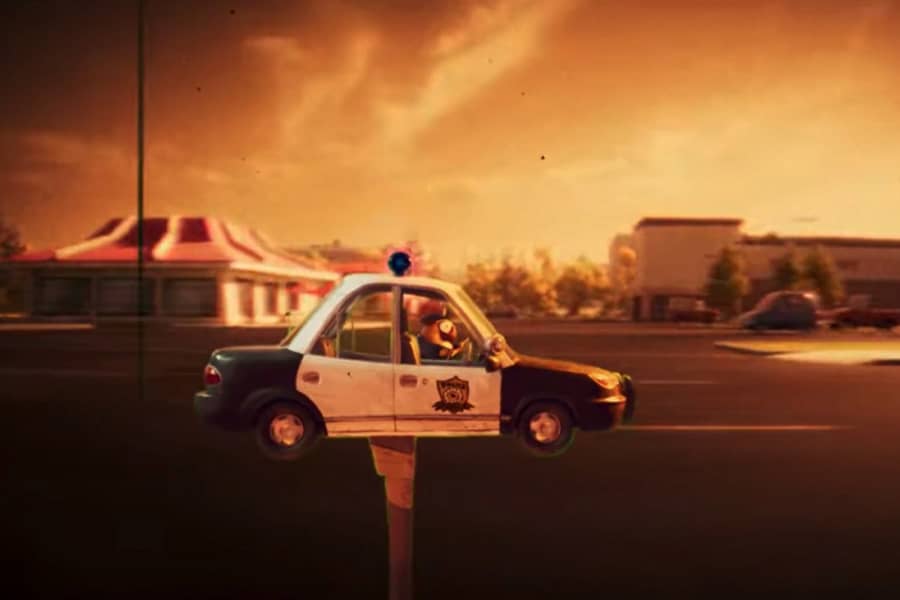 a model cop car on a stick drives in front of a street backdrop