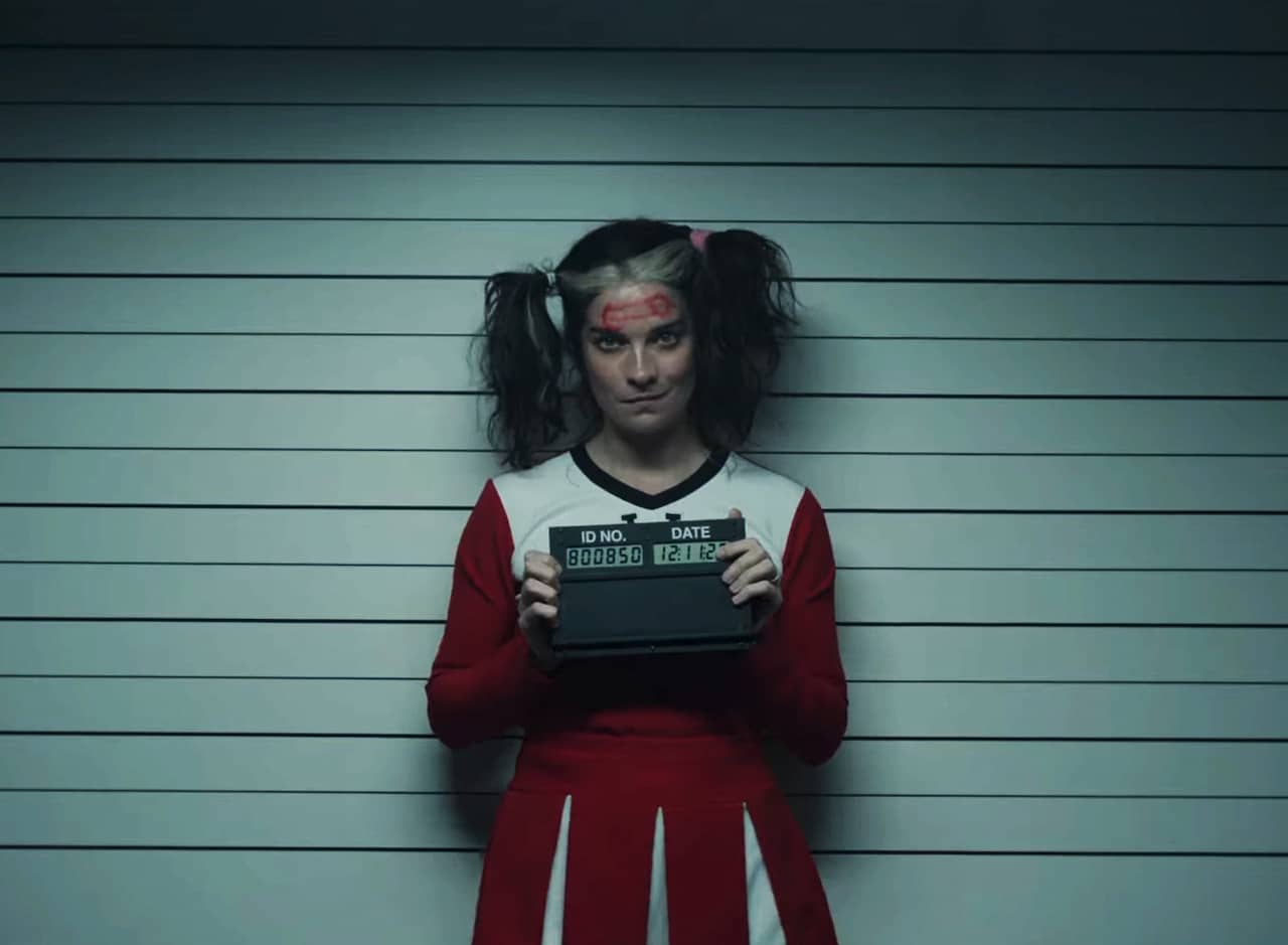 Annie Murphy as Joan, dressed in a cheerleader uniform and getting her mugshot taken