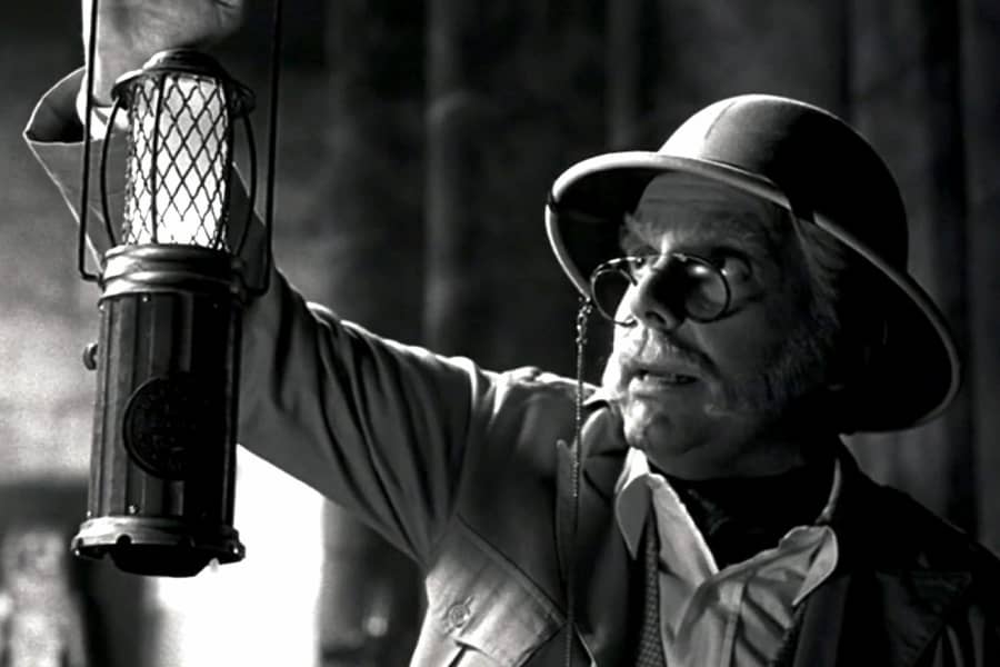 a mustached man holding up a lantern