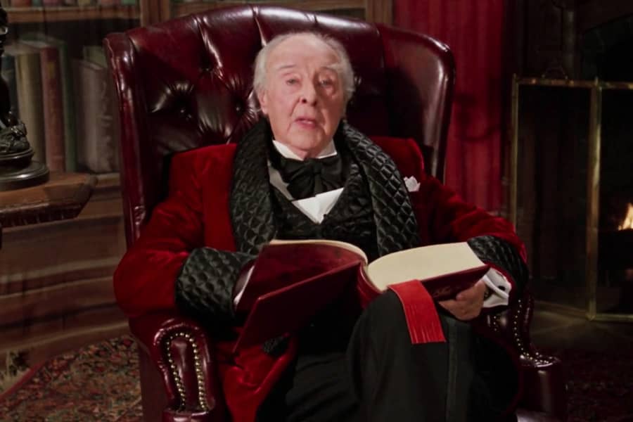 Sir John Houseman in an armchair reading to us