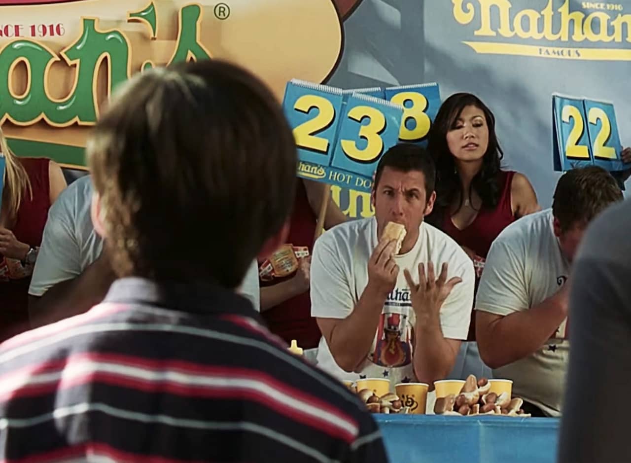 at the hot dog eating contest, a frantic George Simmons shoves a hotdog in his face while gesturing at a young boy