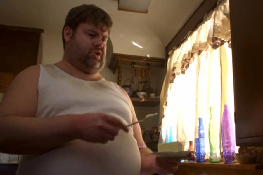 a man holding butter and a knife looks at a toaster