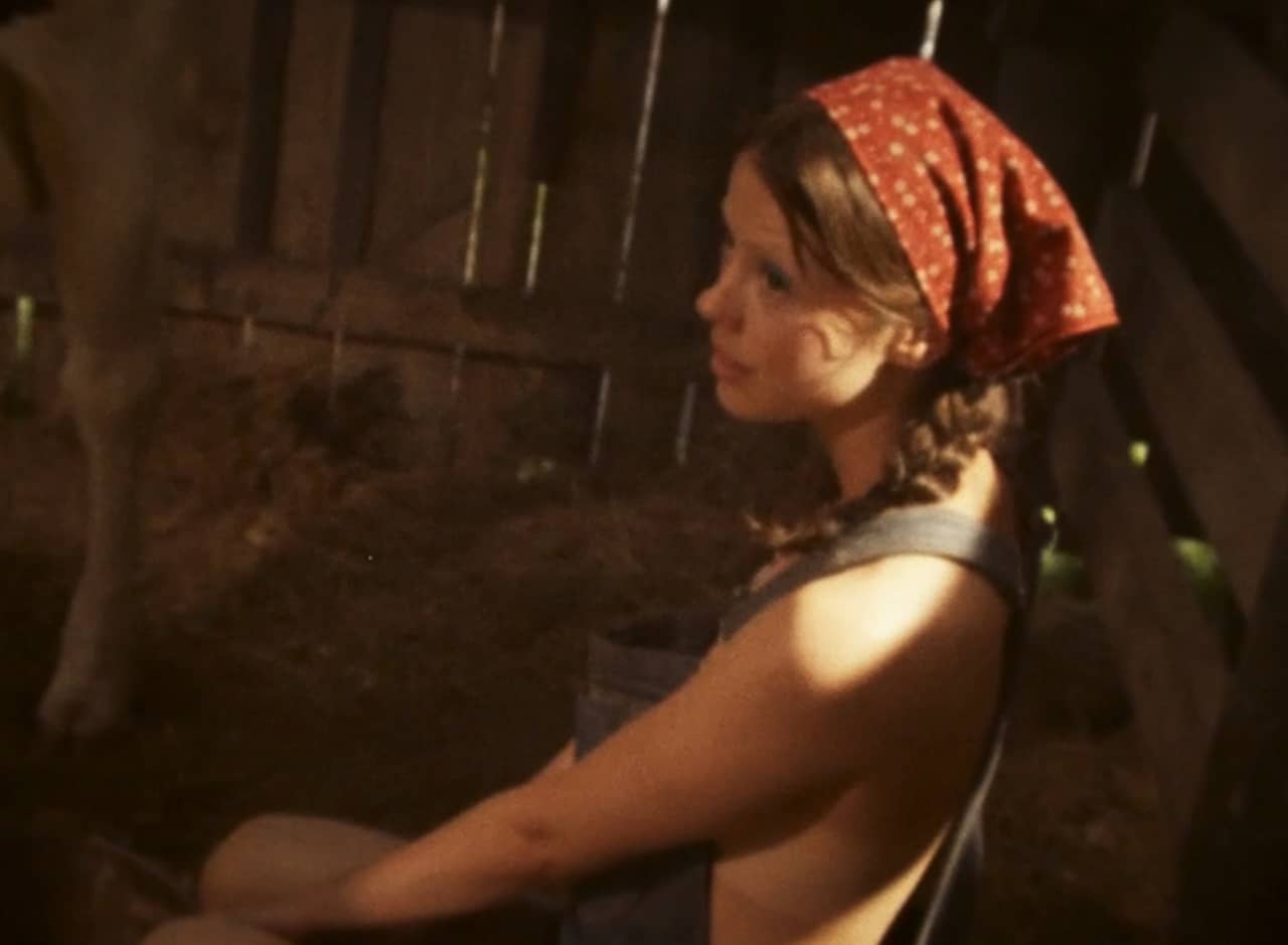 young woman wearing overalls and bandana milking a cow