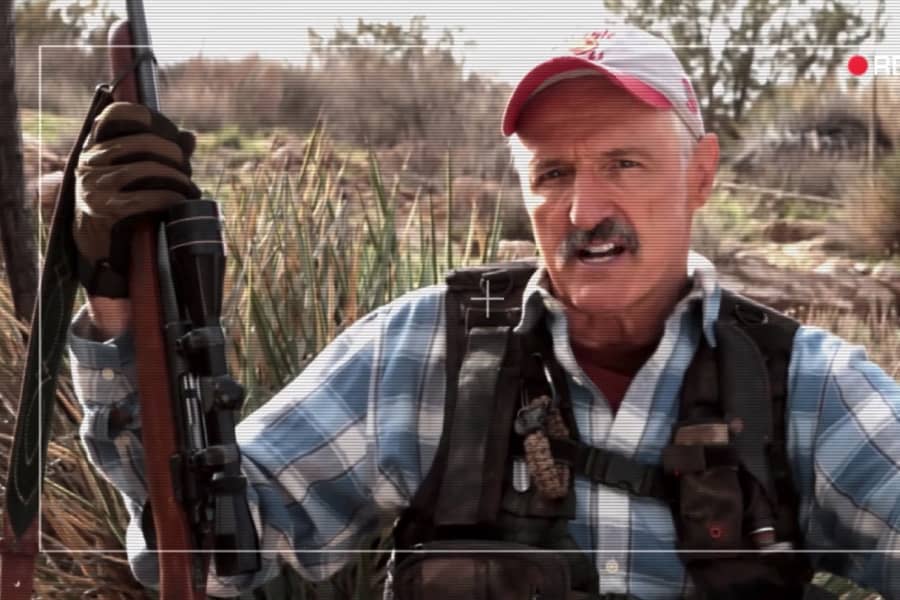 Gummer speaks to the camera holding a gun