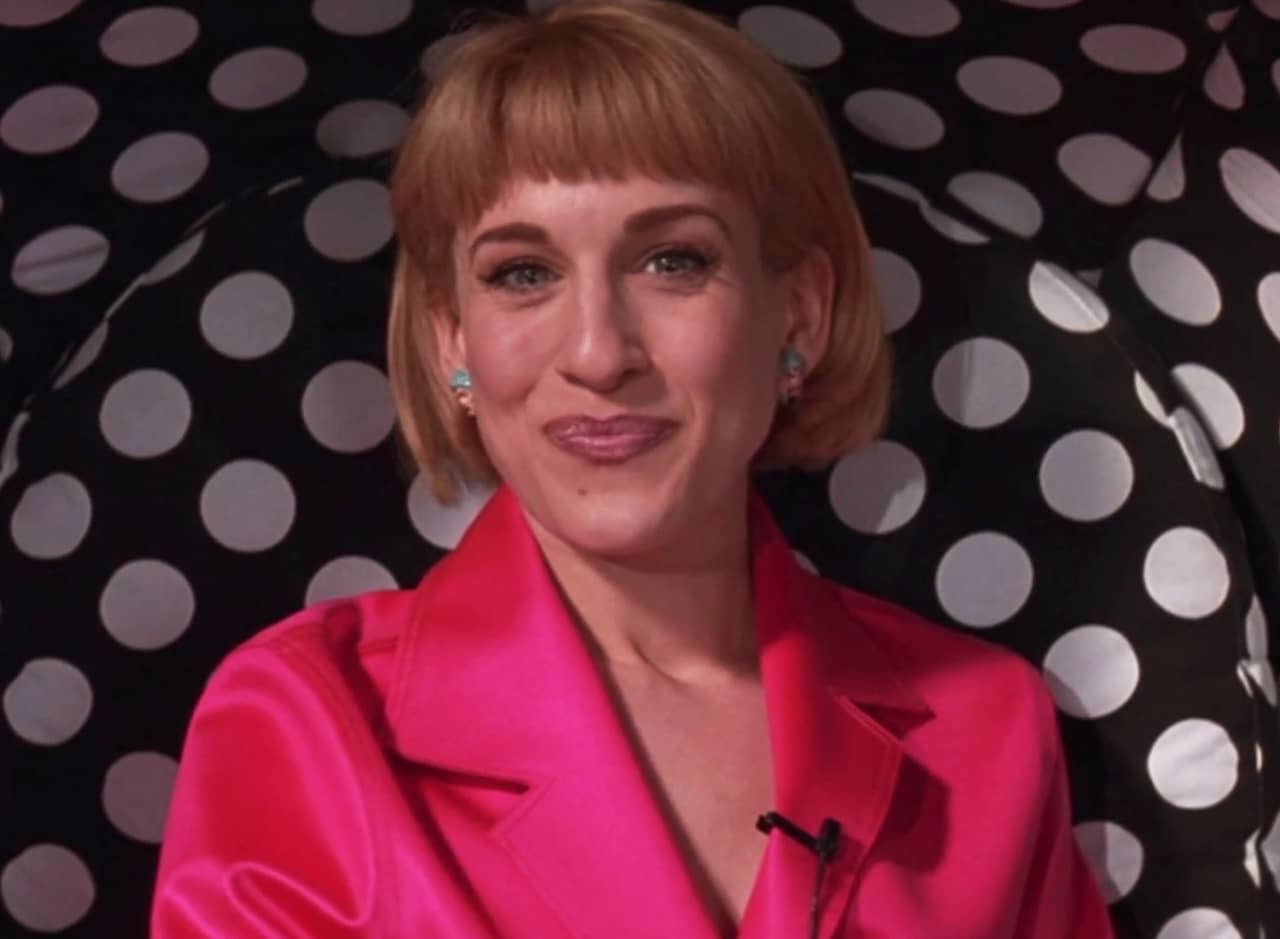 Nathalie Lake smiles in a pink suit and polka dot backdrop