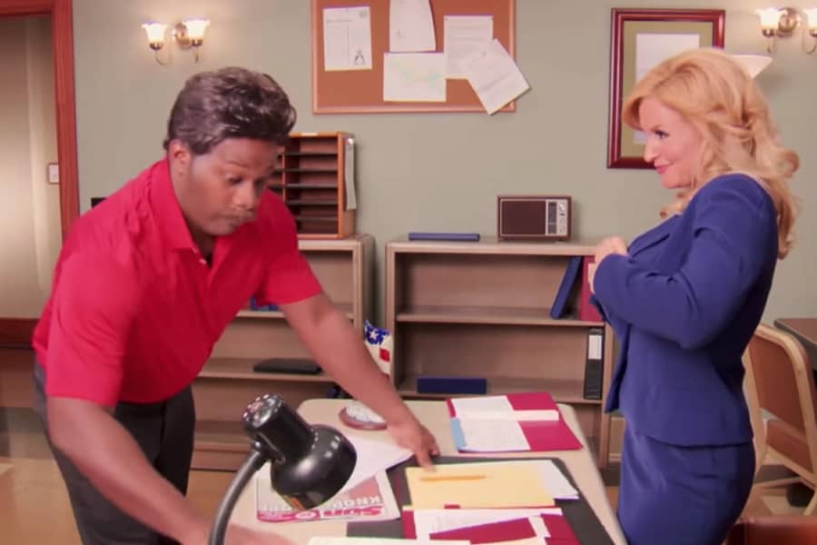 Dong clears papers off the desk as Leslie unbottons her jacket