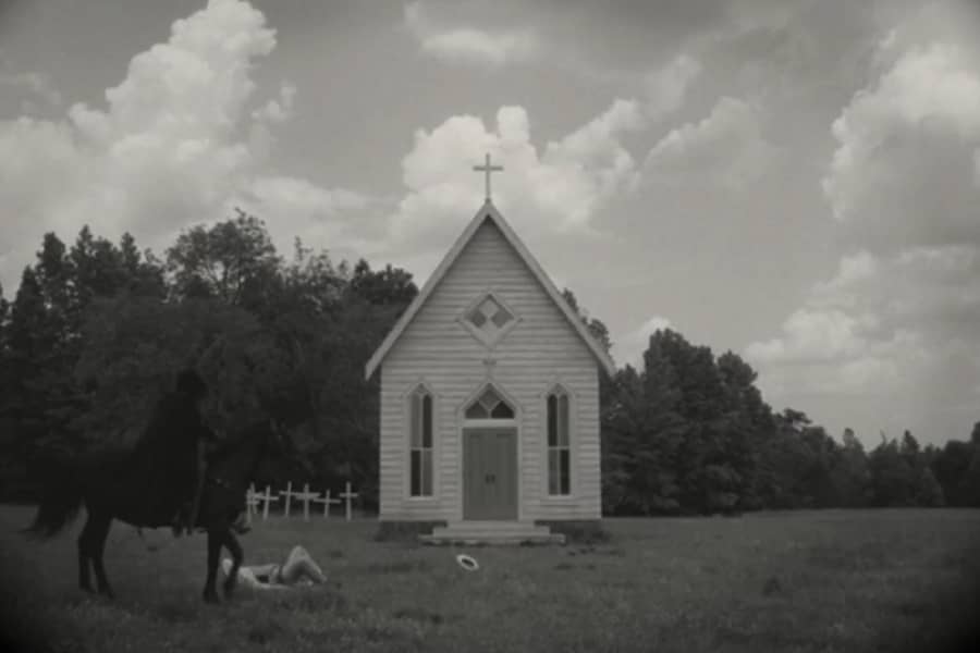 the hooded horse rider captures a man on the ground in front of a small church